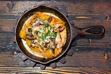 An old frying pan with fried potatoes, mushrooms and sauce. Flat lay. Homemade food, rustic cuisine
