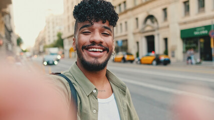 Young happy man with beard, dressed in an olive-colored shirt, stands next to the road, smiles and...