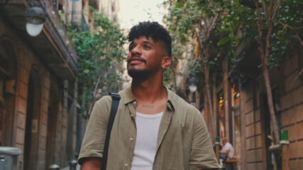 Close up, young smiling man dressed in an olive-colored shirt walks along the narrow street of the...
