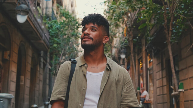 Close up, young smiling man dressed in an olive-colored shirt walks along the narrow street of the old city and looks around