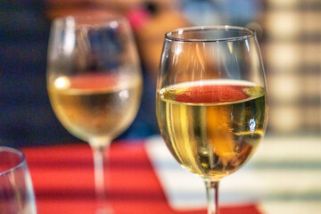 Two glasses of white wine standing side by side in a close up view over a restaurant abstract background