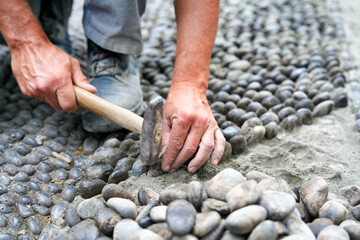 Road works. Man puts pebbles on the old road with the hammer
