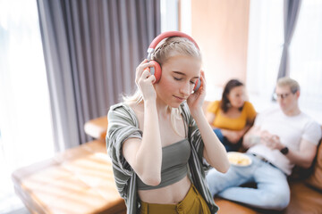 Happy young girl uses headphones to listen to music while relaxing at home with her family, and a gorgeous smiley woman enjoys her pastime and leisure time in the entertainment room. - obrazy, fototapety, plakaty