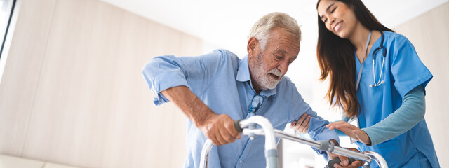 Portrait of Asian young nurse helping old elderly disable man grandfather to walk by using walker equipment in the bedroom. Senior patient of nursing home moving with walking frame and nurse support - obrazy, fototapety, plakaty