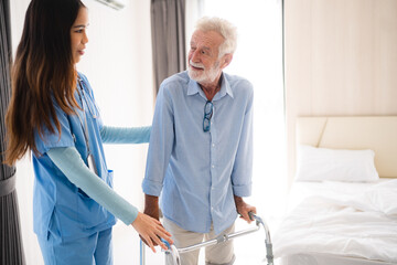 Fototapeta premium Portrait of Asian young nurse helping old elderly disable man grandfather to walk by using walker equipment in the bedroom. Senior patient of nursing home moving with walking frame and nurse support