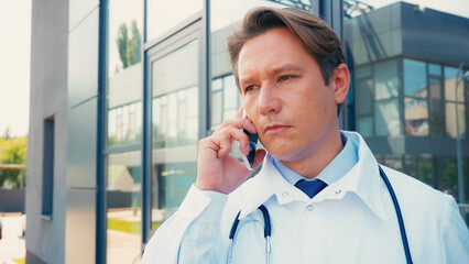 serious doctor talking on mobile phone near city hospital outdoors.