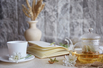 Organic linden tea in teapot with cup of tea. Wheat, chrysanthemums, autumn decorations and notebook. Cozy atmospheric relax at home.