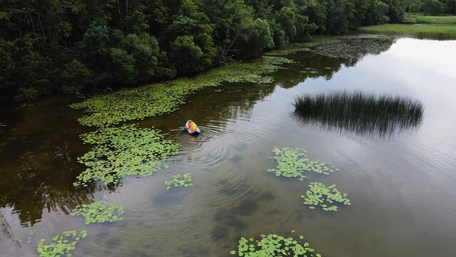 male fisherman in an orange raincoat floats on an inflatable boat on the lake in summer. drone point of view