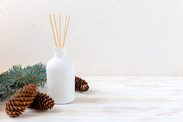 Aromatic reed diffuser with sticks on a white background with a Christmas tree branch and cones