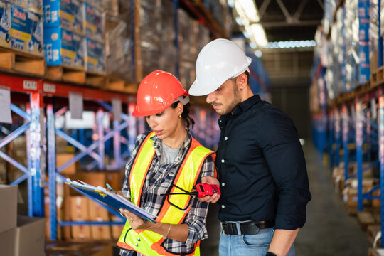 Male foreman looking at checklist report and discussing with female worker at the warehouse factory. Logistics worker checking at stock distribution before shipping delivery.