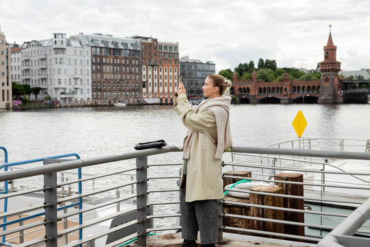 Side view of young woman taking photo on pier in Berlin.