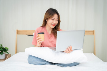 Asian woman sitting at home working in bedroom or home office drinking coffee cheerful and having fun at work