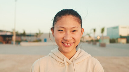 Close up, asian girl in sportswear stands at morning time on modern buildings background and looks at the camera