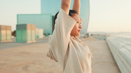 Fototapeta na wymiar Asian girl in sportswear doing workout at morning time, stretching on modern buildings background