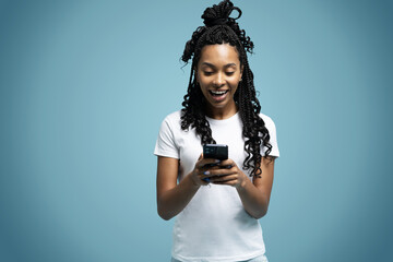 Curly haired ethnic woman uses mobile phone checks messages holds modern cellular in hands isolated over blue background
