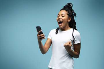 Curly haired ethnic woman uses mobile phone checks messages holds modern cellular in hands isolated over blue background