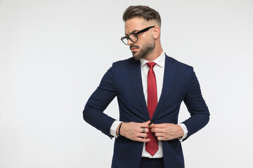 bearded elegant businessman with red tie buttoning suit and looking to side