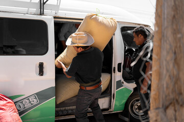A Hispanic farmer is unloading a coffee sack from a van