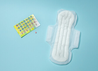 Birth control pills and a white sanitary pad lie on a light blue background. Menstrual cycle and pregnancy. Negative pregnancy test and contraceptives