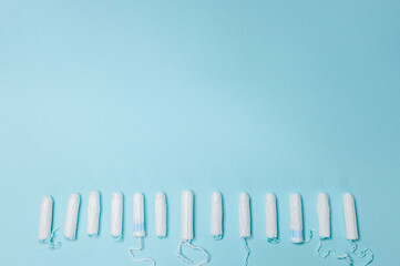 Many sanitary tampons lie in a row on a light blue background. Menstrual cycle and pregnancy. Negative pregnancy test and contraceptives