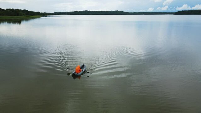 male fisherman in an orange raincoat floats on an inflatable boat on the lake in summer. drone point of view