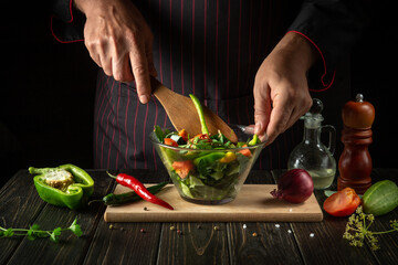 The chef cooks a delicious vegetable salad. Vegetarian food by hands of the cook in the kitchen. Menu idea for a hotel or restaurant.