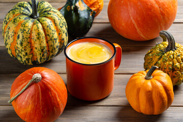 Pumpkin cream soup served in orange cup. Mug  of autumn soup and different varieties of pumpkins on...