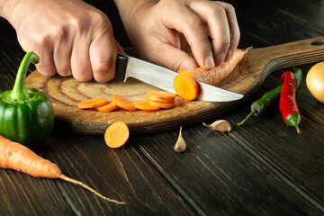 The cook cuts carrots on a cutting board for preparing a vegetarian lunch or breakfast. Delicious healthy food