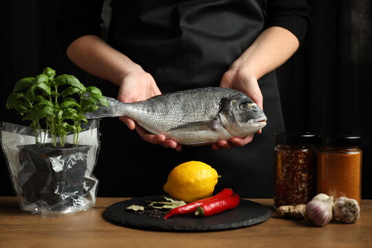 The chef prepares dorado on a black background, raw fish with spices.