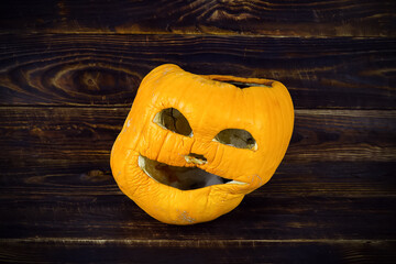 Stale halloween pumpkin on wooden board surface, jack o lantern face wilted - obrazy, fototapety, plakaty