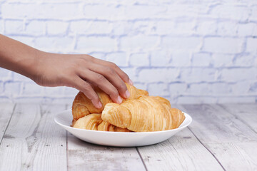person hand picking fresh baked croissant on plate with copy space 