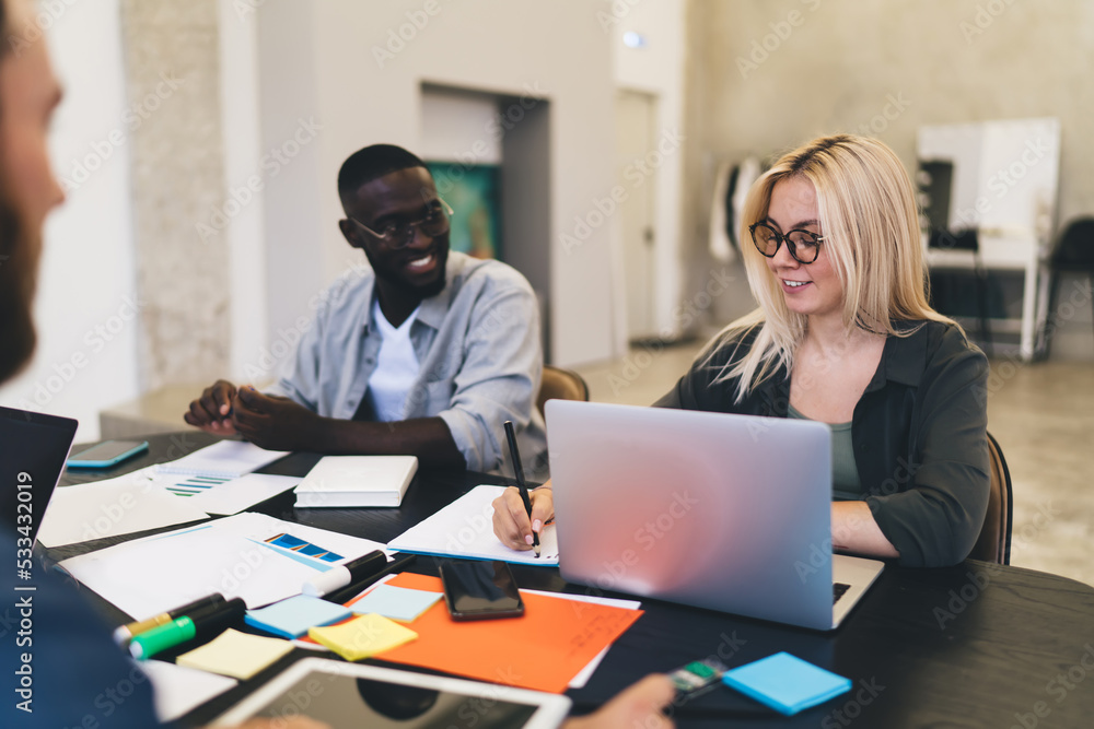 Poster diverse colleagues working on project in office while sitting at table