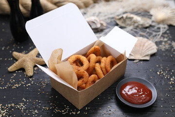 Deep fried squid rings and a tomato sauce, ketchup. Panko calamari in a takeaway carton box, on a...