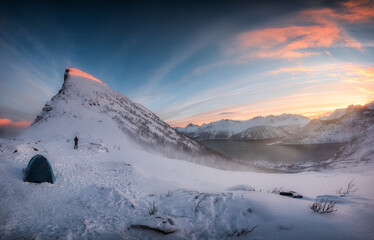 Panorama of sunrise over snowy mountain range with mountaineer tent camping in winter on Segla...