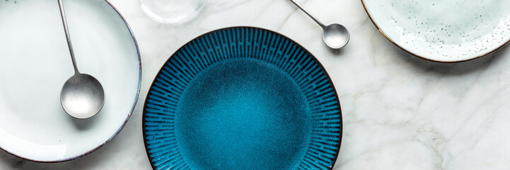 Modern tableware panorama with a vibrant blue plate and cutlery, overhead flat lay shot. Trendy...