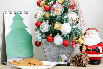 Countdown to Christmas concept, Christmas December calendar besides Christmas tree, Santa Claus figurine, snow globe, pine and a plate of festive gingerbread biscuits