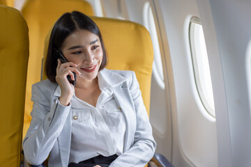 Young Asian business woman talking on smartphone, businesswoman working while flying at plane, Young woman using the internet at airplane, Air travel, long flight.