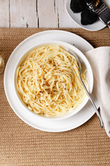 Cacio e Pepe - Italian pasta with grated Pecorino Romano cheese and black pepper, together with spaghetti in a white plate on light wooden background. Close up,  flat lay,  top view, copy space.