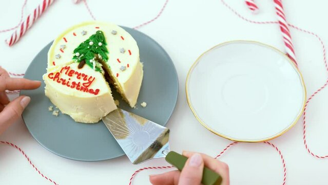Woman hand with a spatula take piece the small bento cake into for holiday. The girl cuts off a piece of a white cake on which there is an inscription Merry Christmas and a Christmas tree cream image