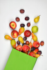 Light green paper bag full of ripe apples ,plums and pears on white background. Flat lay , top view. Healthy, vitamin , fruit dietary food for life concept. Free copy space.
