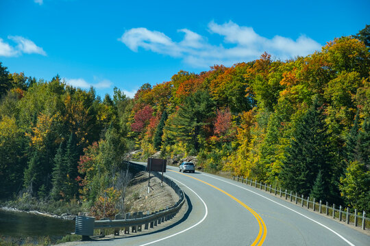 A Car Traveling Along Highway 60 Through Algonquin Park with Fall Colors and Blue Skies as Backdrop