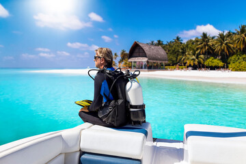 A scuba diver in his diving gear sits in front of a boat and enjoys the view of the tropical...