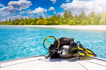 Concept of scuba diving with air tank and equipment lying on a boat in front of a tropical paradise beach with turquoise sea and palm trees