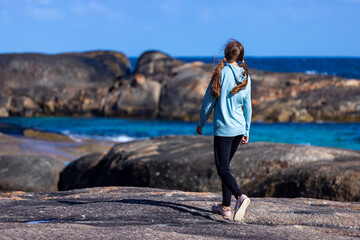girl in ponytails walking along beach with massive rocks in the background, elephant rocks in...
