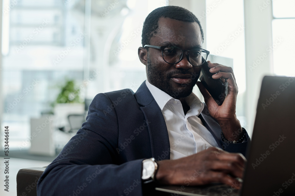 Poster young busy ceo or employee in formalwear speaking by mobile phone and looking at laptop screen while