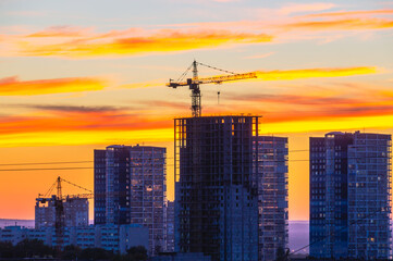 Red sunset and blue sky with a view of the houses in the city. Tower cranes and houses under construction in the city at sunset.  A bright red sunset with heavy dark clouds. An impending hurricane.