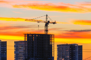 Red sunset and blue sky with a view of the houses in the city. Tower cranes and houses under construction in the city at sunset.  A bright red sunset with heavy dark clouds. An impending hurricane.