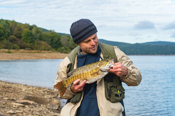 man with big bass trophy fish fall season catch, smallmouth bass copy space background image, happy...