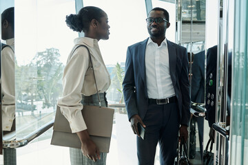 Young elegant woman with handbag and her colleague in suit having discussion of some working points in moving elevator © pressmaster