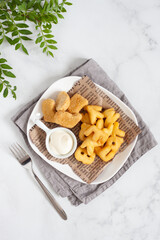 A dish for young children - nuggets, mashed potatoes in the form of an alphabet and cream sauce. Colorful dinner on a white table. A plate taken from above (top view, flat position).